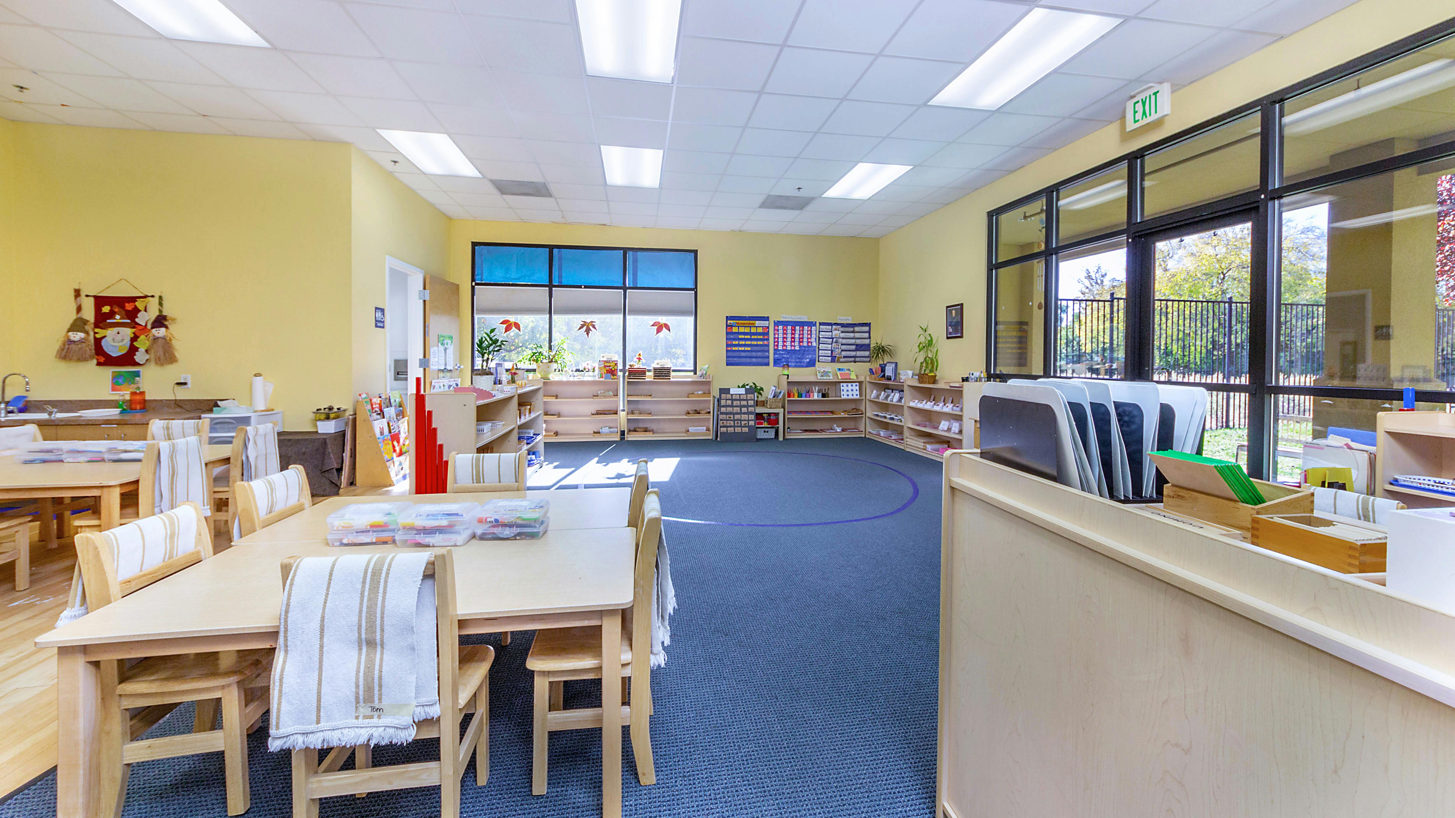 Classroom with small tables and chairs, shelves, and large windows