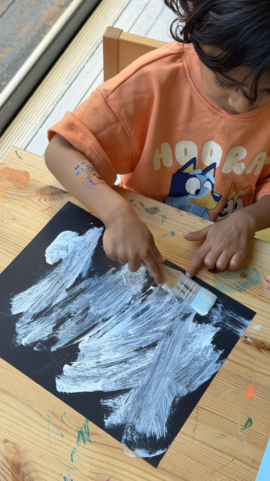 Child painting white strokes on black paper with a brush