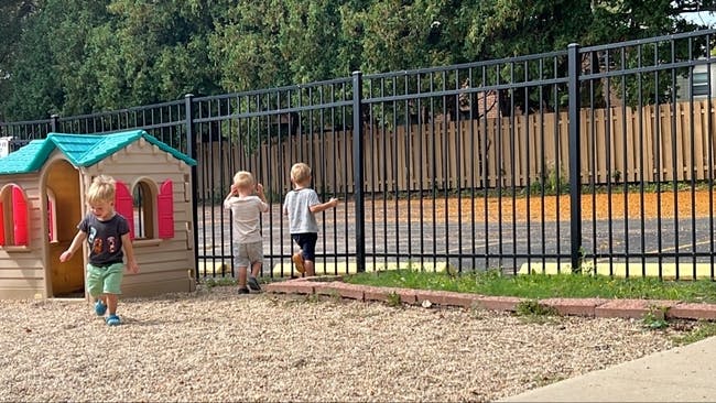 Three children playing near a playhouse and fence