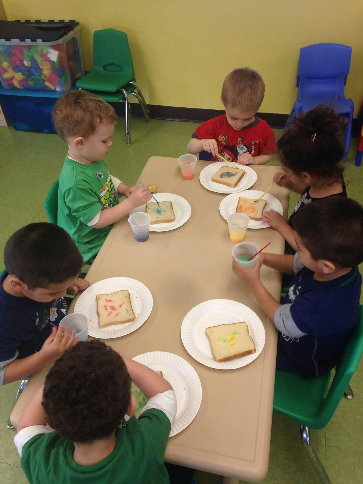 Children painting on slices of bread at a table in a classroom