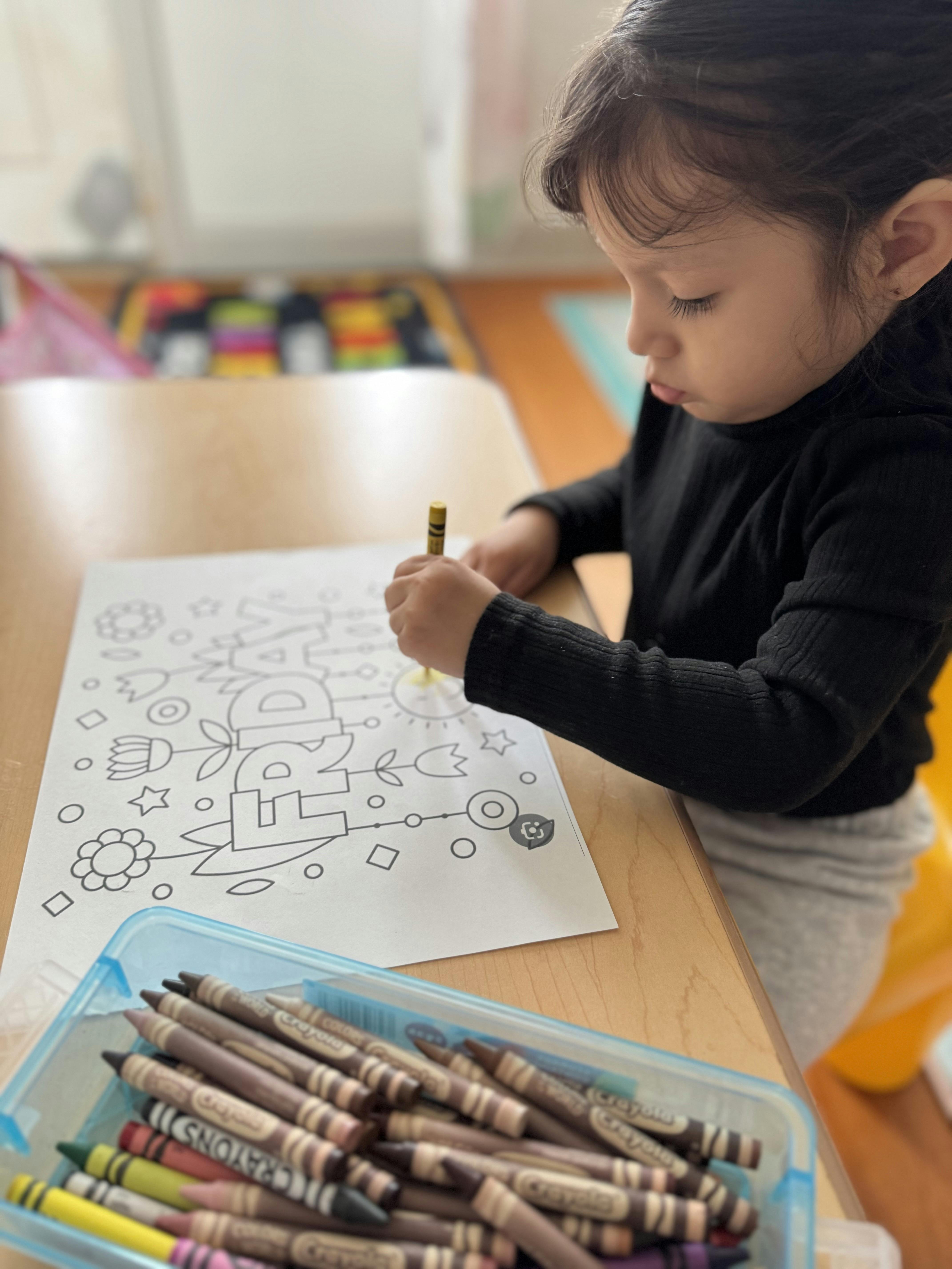 Child coloring a picture with a crayon at a table