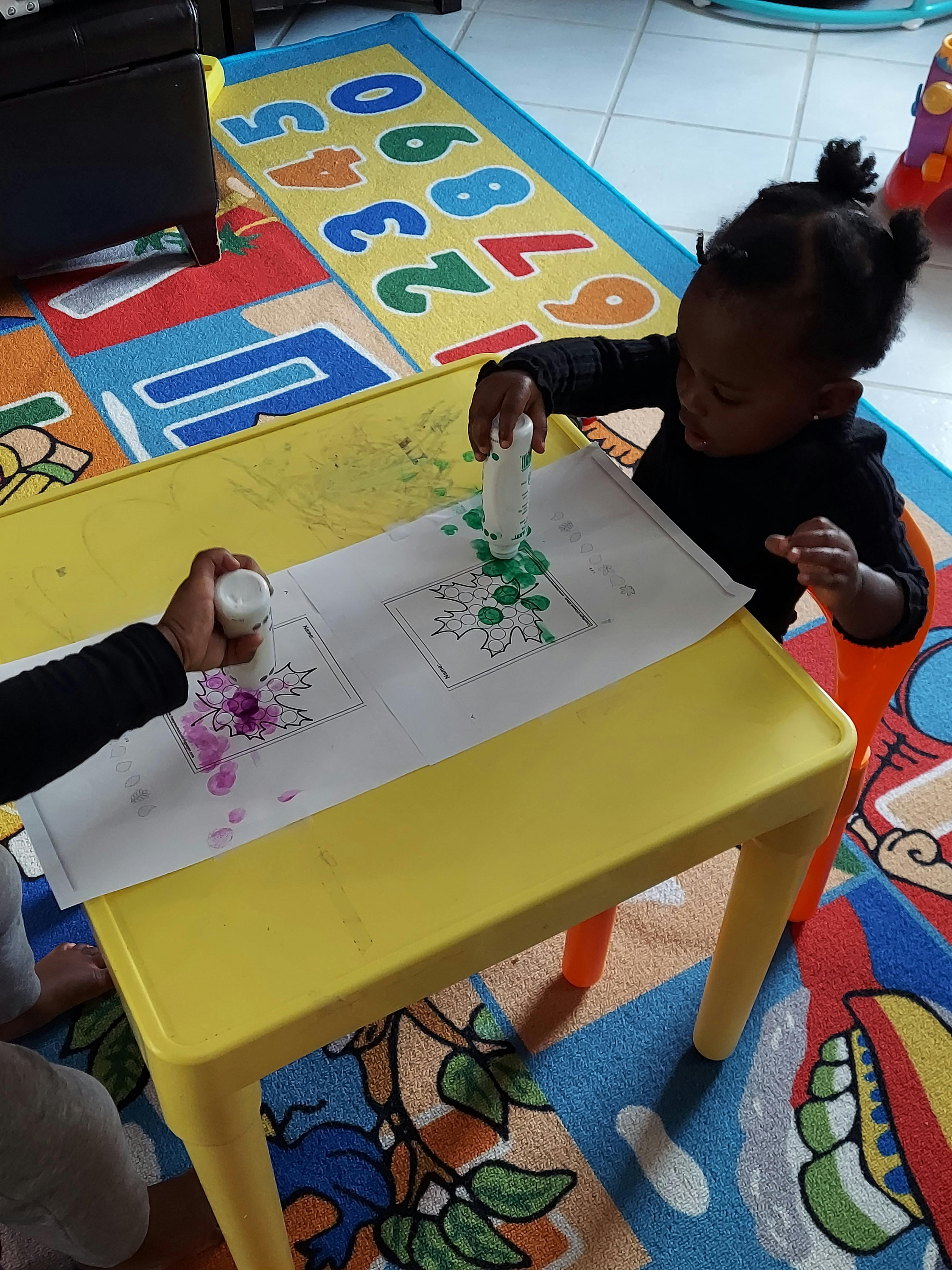 Two children making art with paint daubers at a yellow table