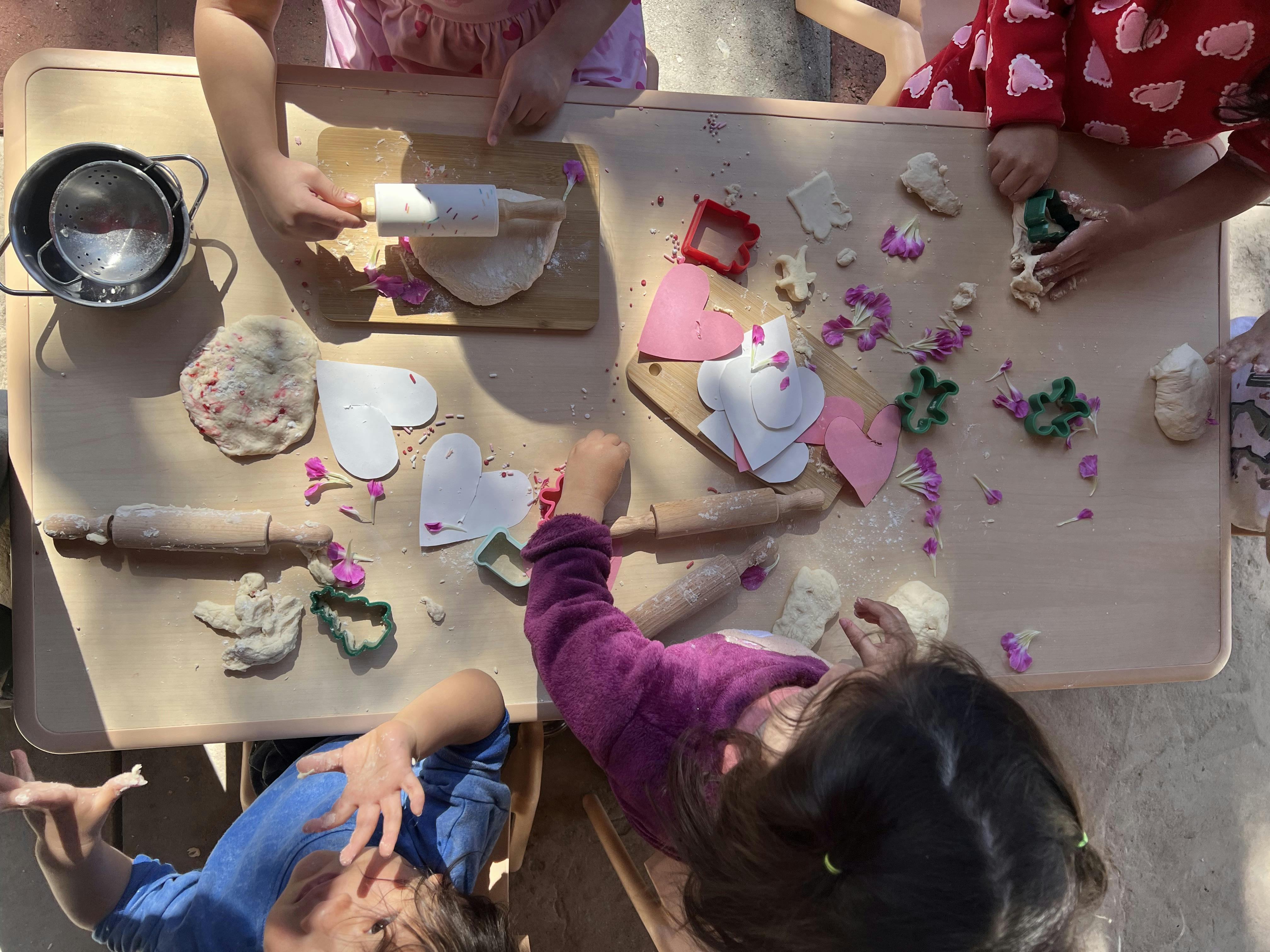 Children using rolling pins and cutters to shape dough on a table
