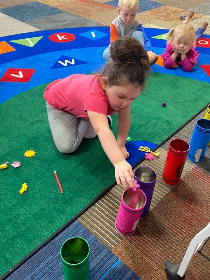 Child playing with cans on a rug, with other children in the background