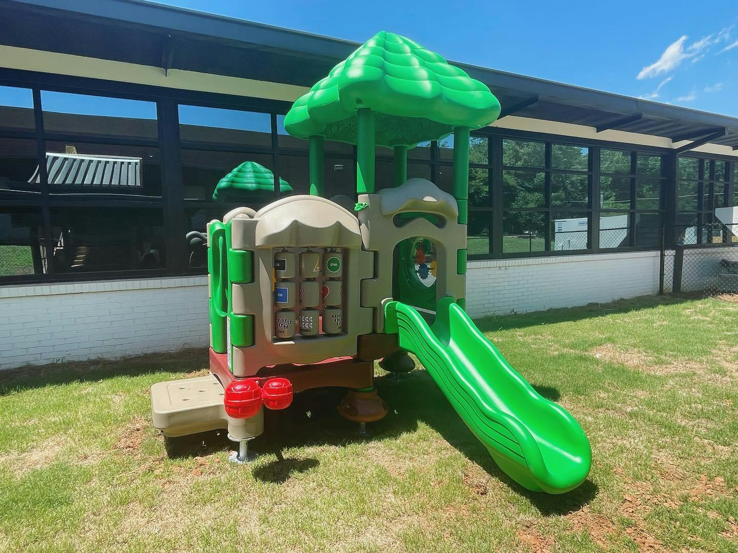 Playground structure with a green slide on grass