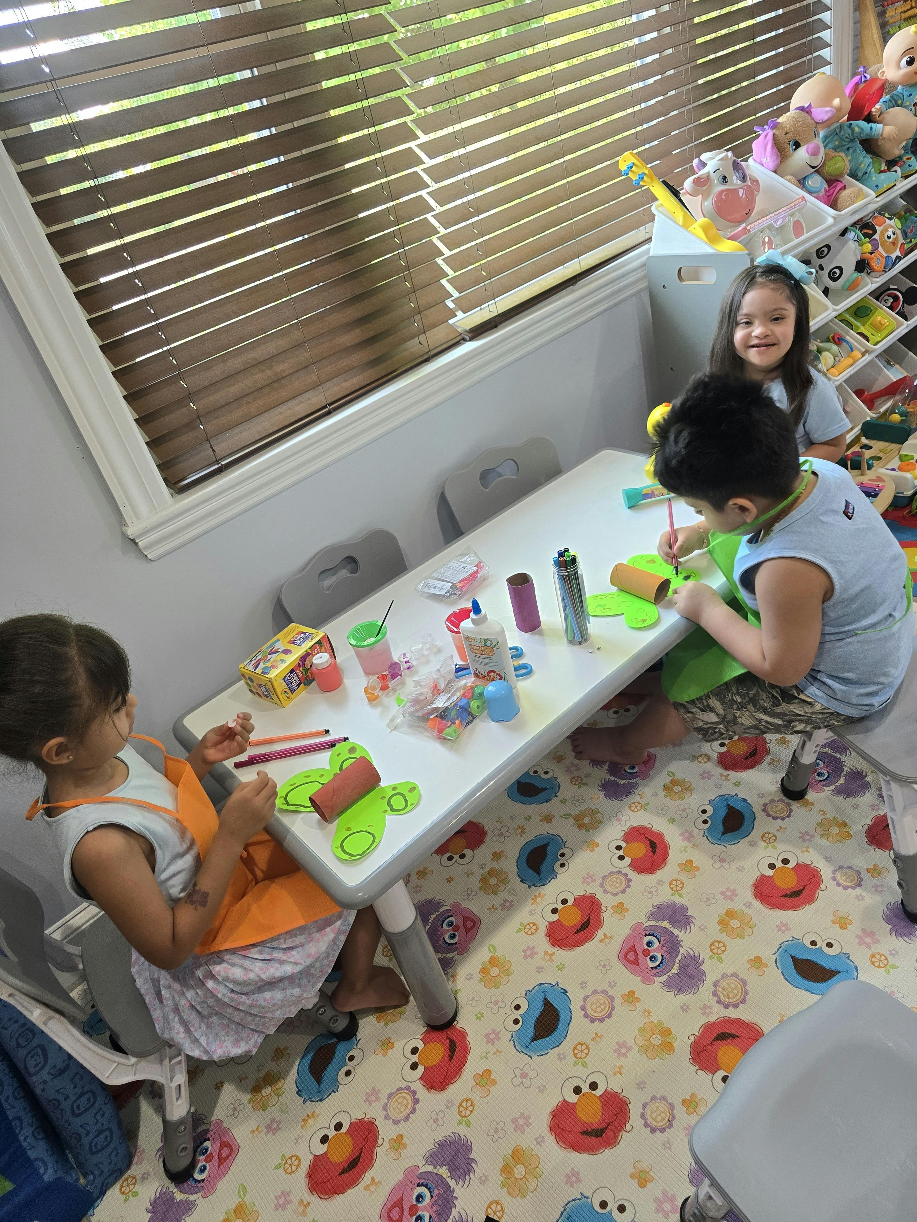 Three children sitting at a table crafting with paper and art supplies