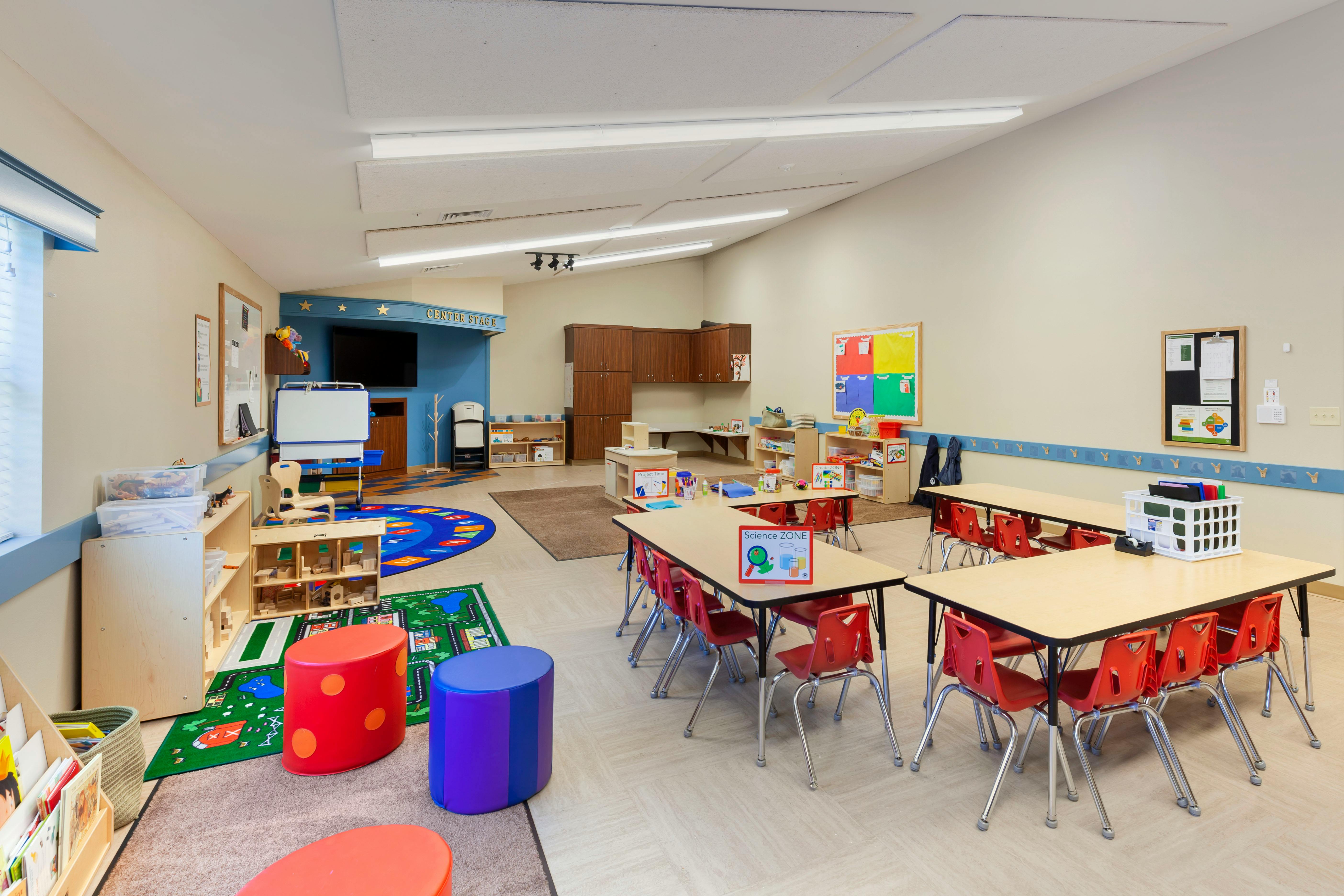 Colorful classroom with several activity areas, tables, and red chairs
