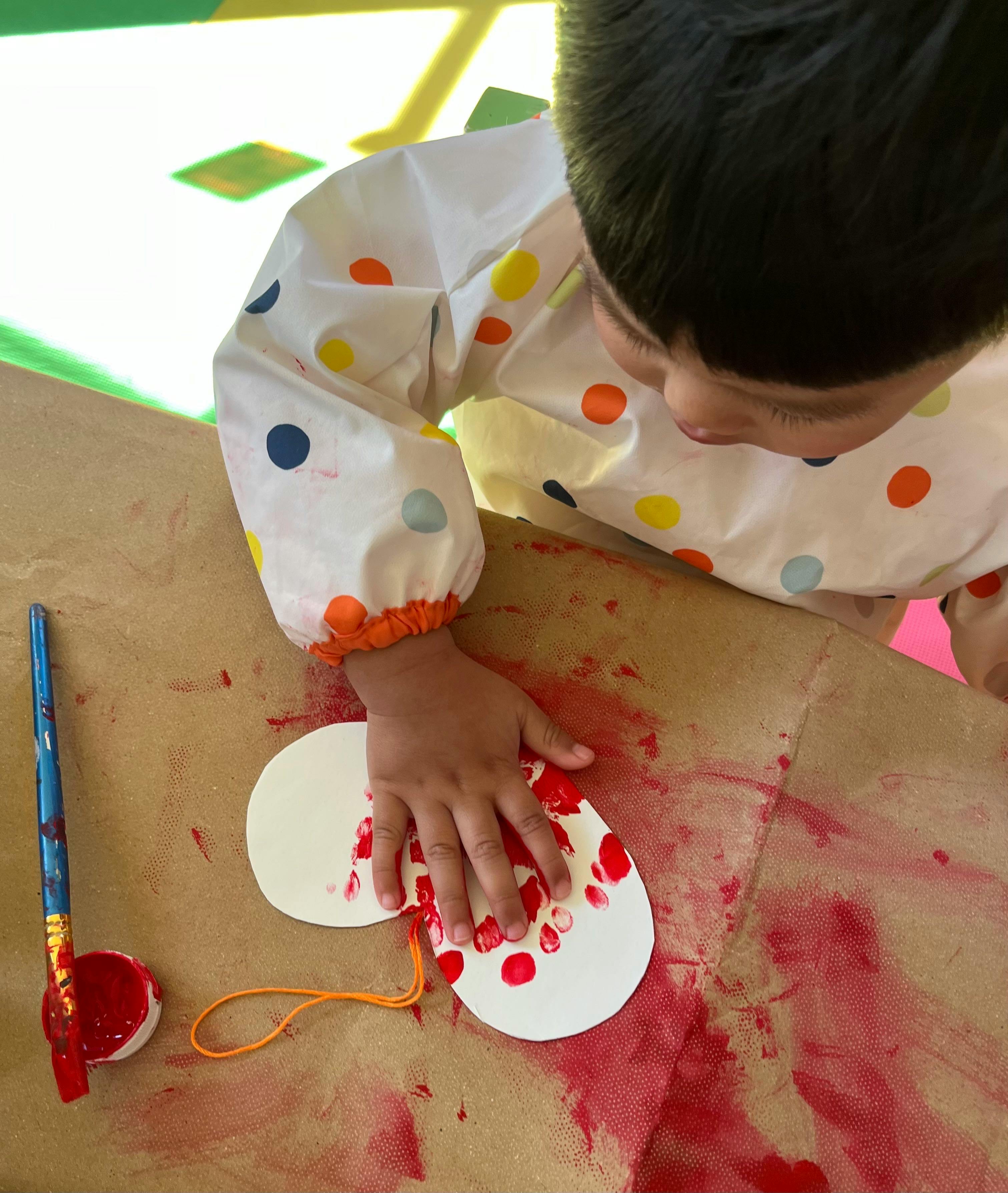 Child painting a white paper shape with red paint