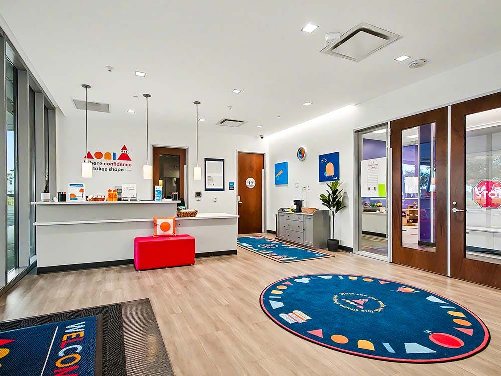 An empty reception area with a counter, a red bench, and two circular rugs