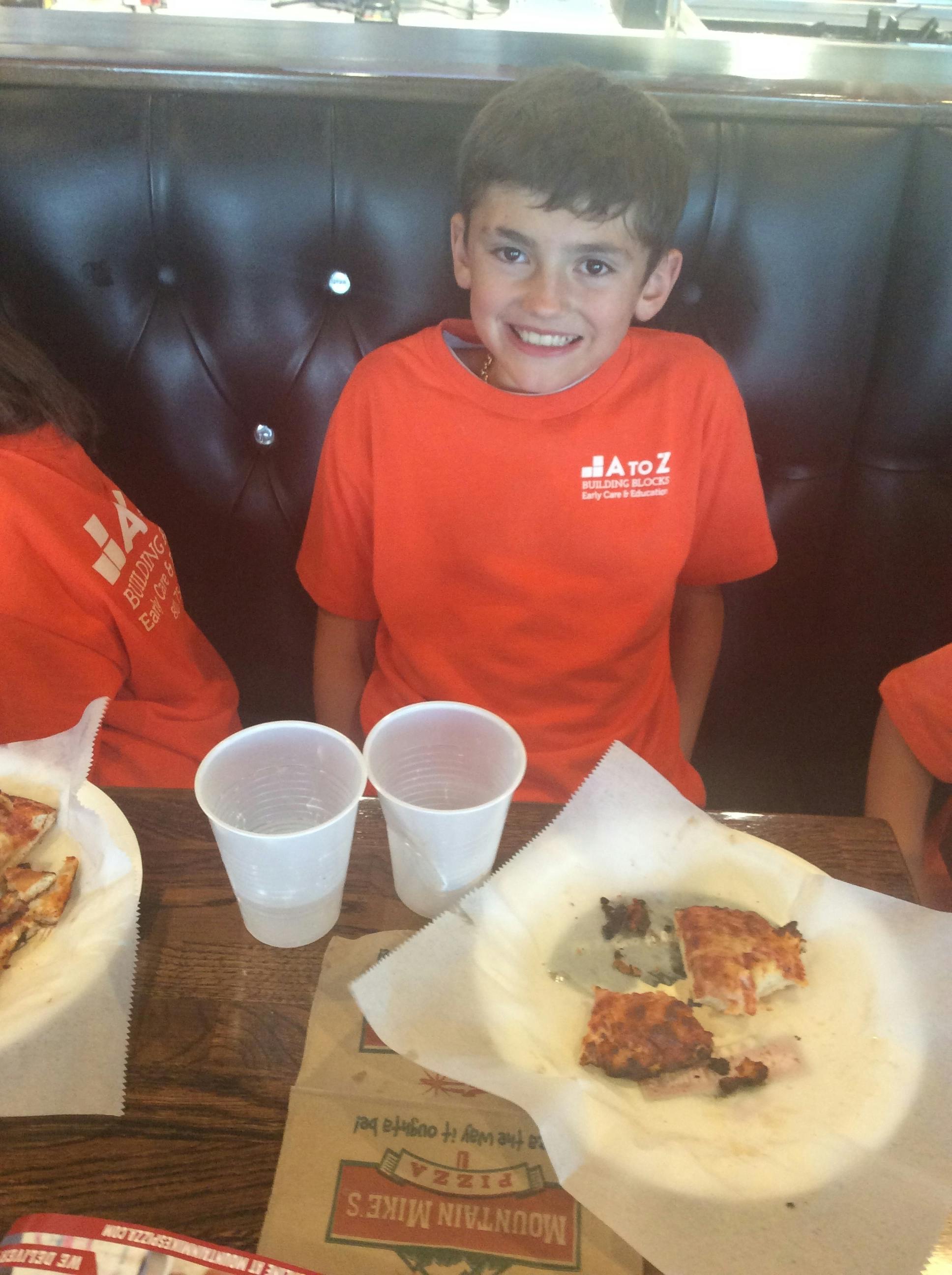 Child wearing an orange A to Z t-shirt sitting at a restaurant table with pizza