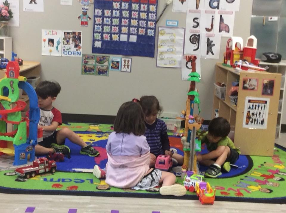 Children playing with toys on a colorful rug in a classroom