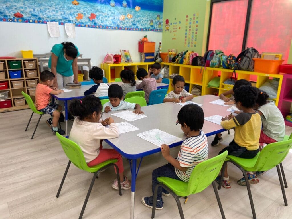 Adult and children sitting at tables in a classroom