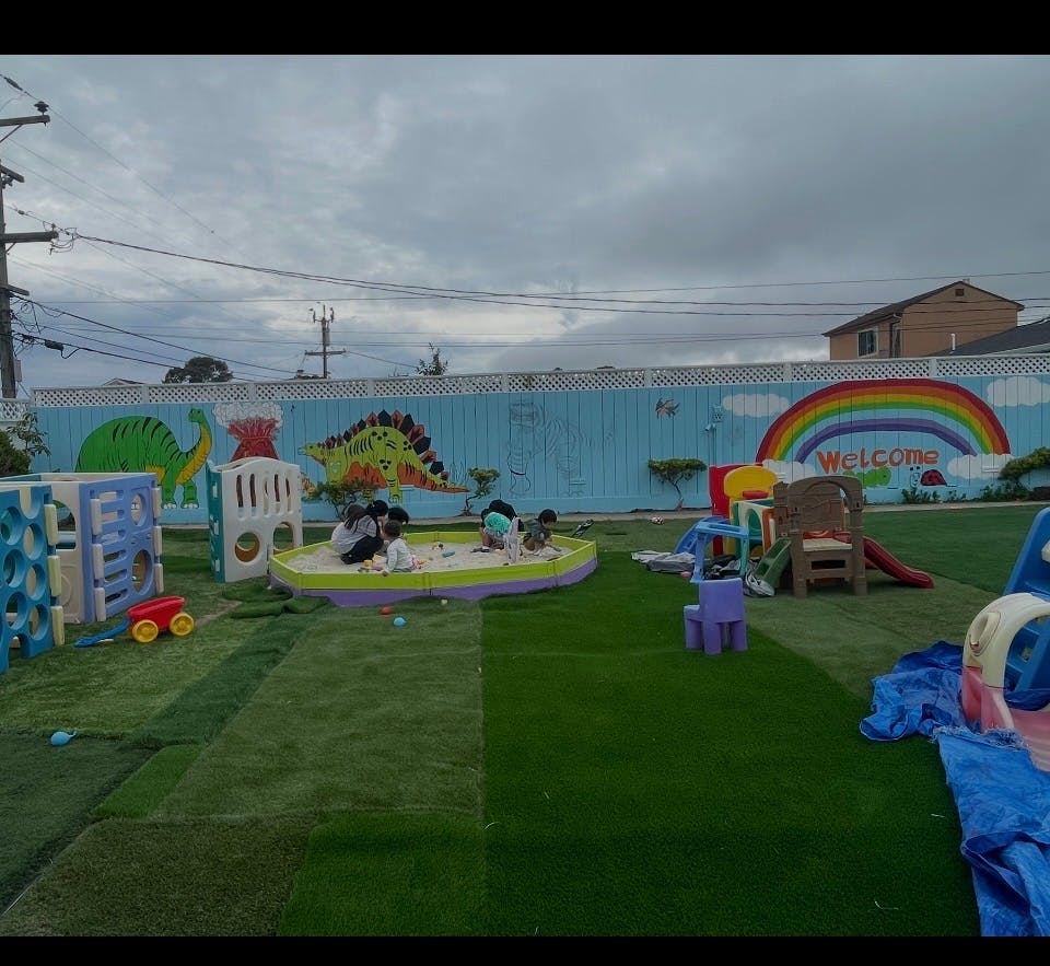 Children playing in a sandbox in a playground with a painted fence