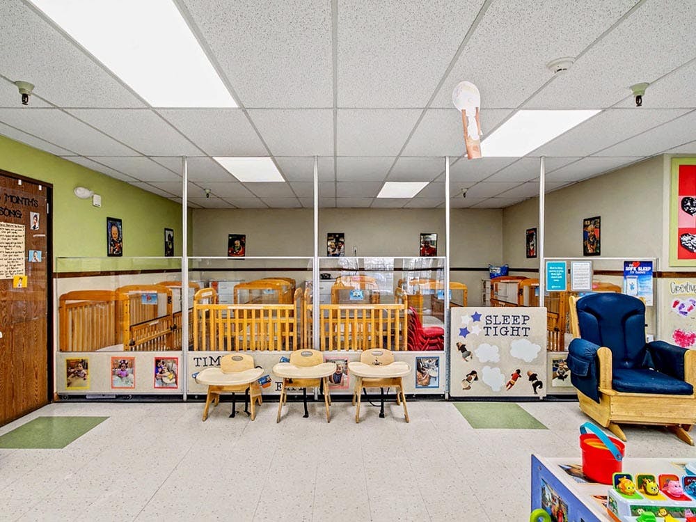 Cribs in a daycare room separated by clear partitions