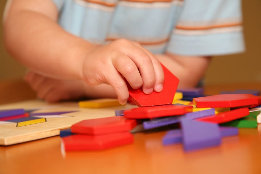 Child's hand holding a red geometric shape block