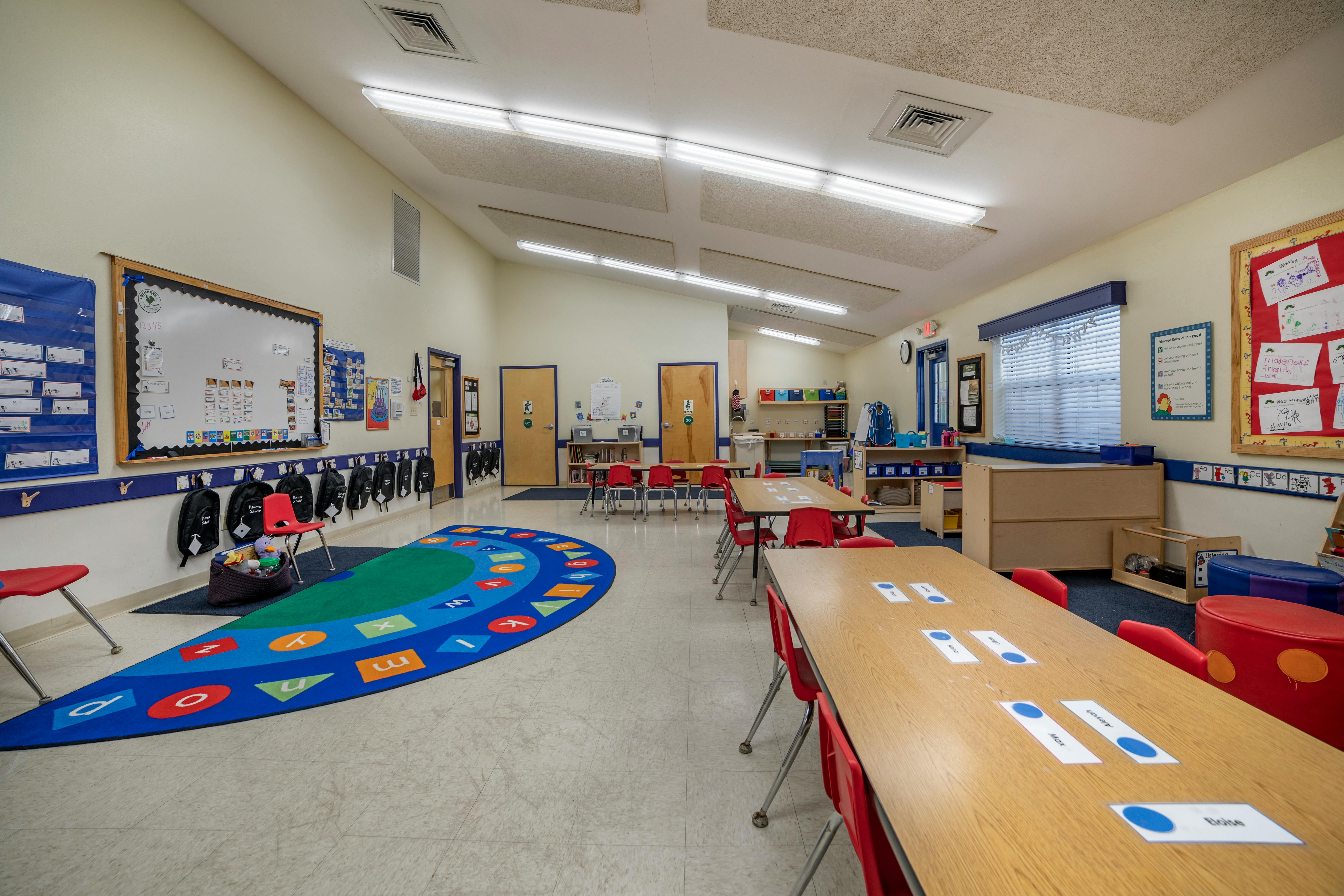 An empty classroom with small tables, chairs, and an alphabet rug