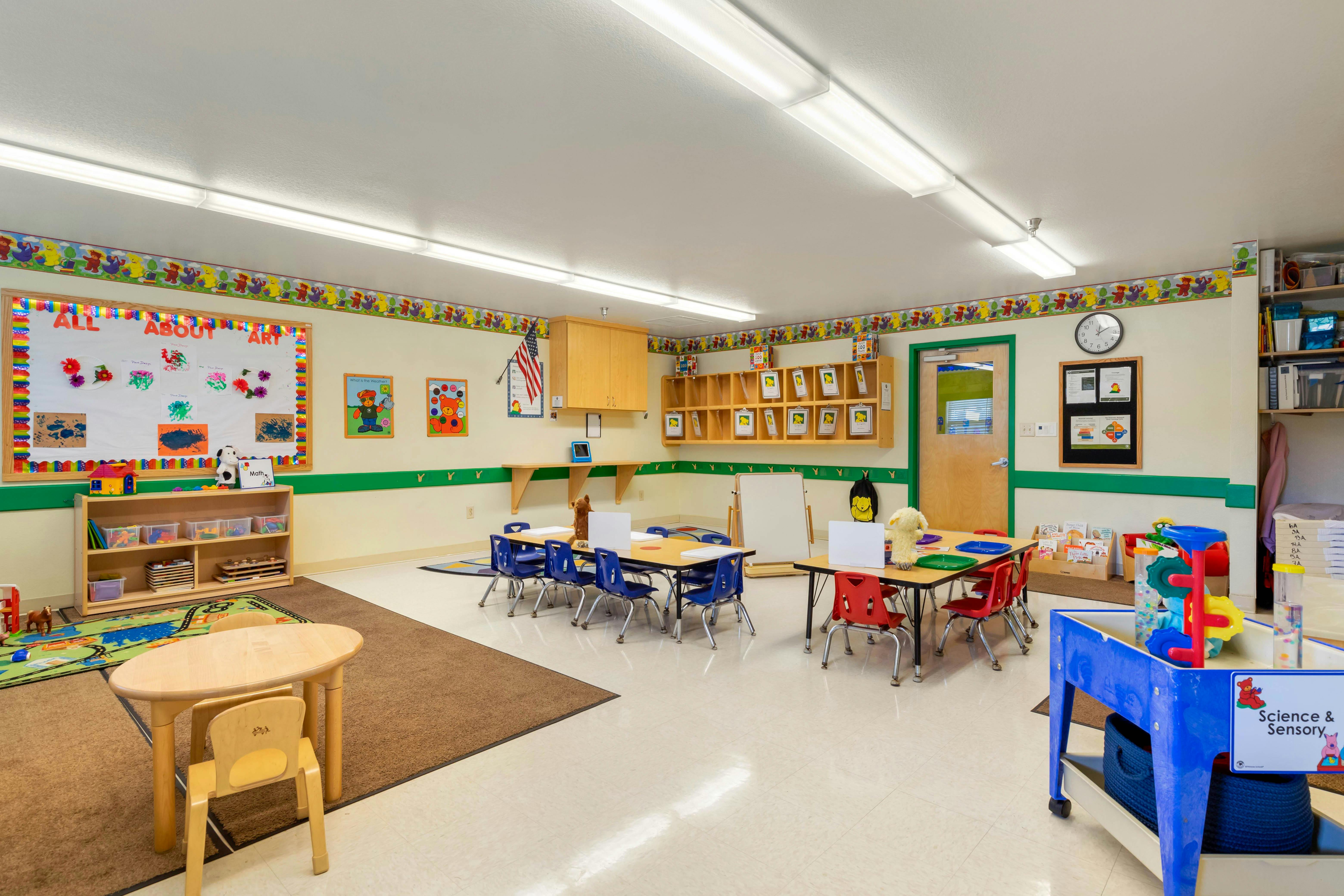 Classroom with small tables and chairs, art display, and cubbies