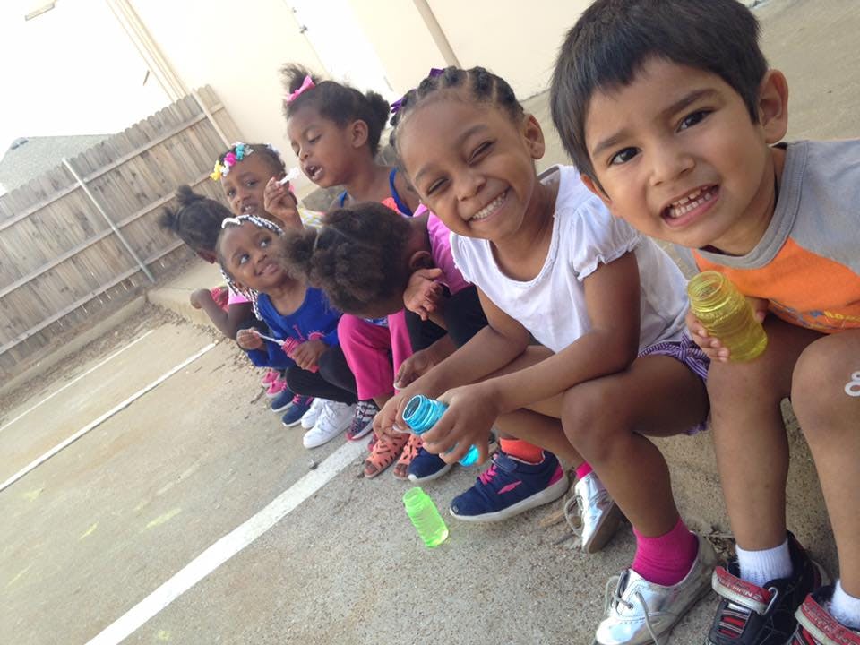 Group of children sitting in a row, some holding bubble wands