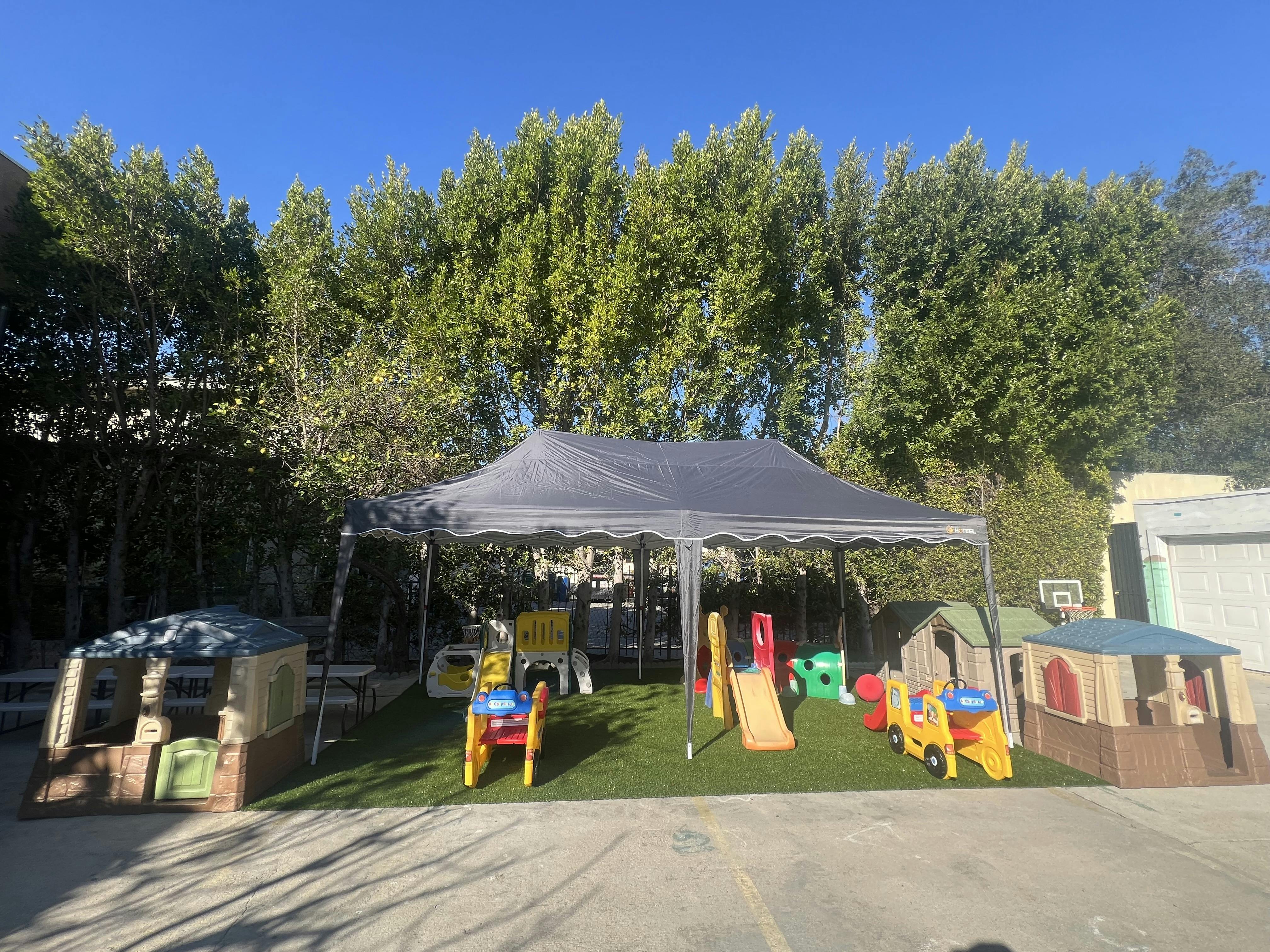 Outdoor play area with a canopy, slides, and playhouses on artificial turf