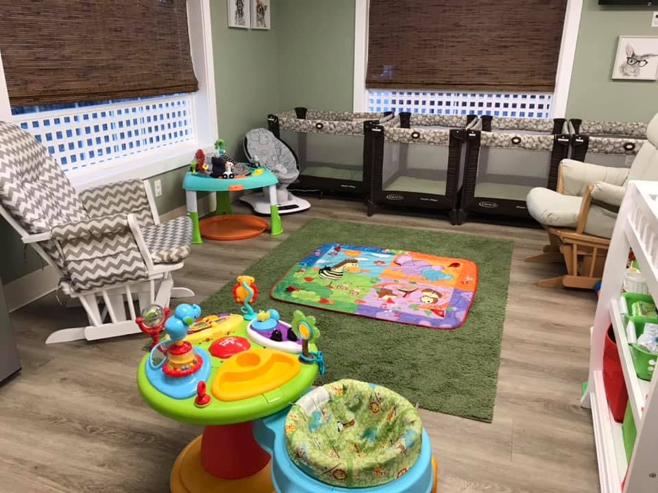 Nursery room with multiple cribs, a rocking chair, and infant play items