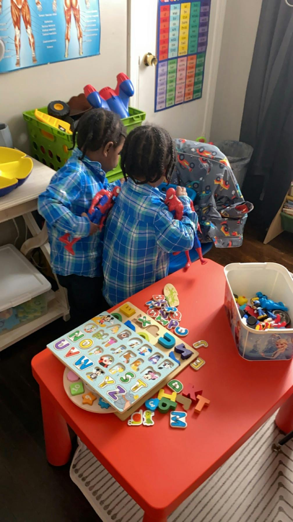 Two children playing with toys and an alphabet puzzle on a red table