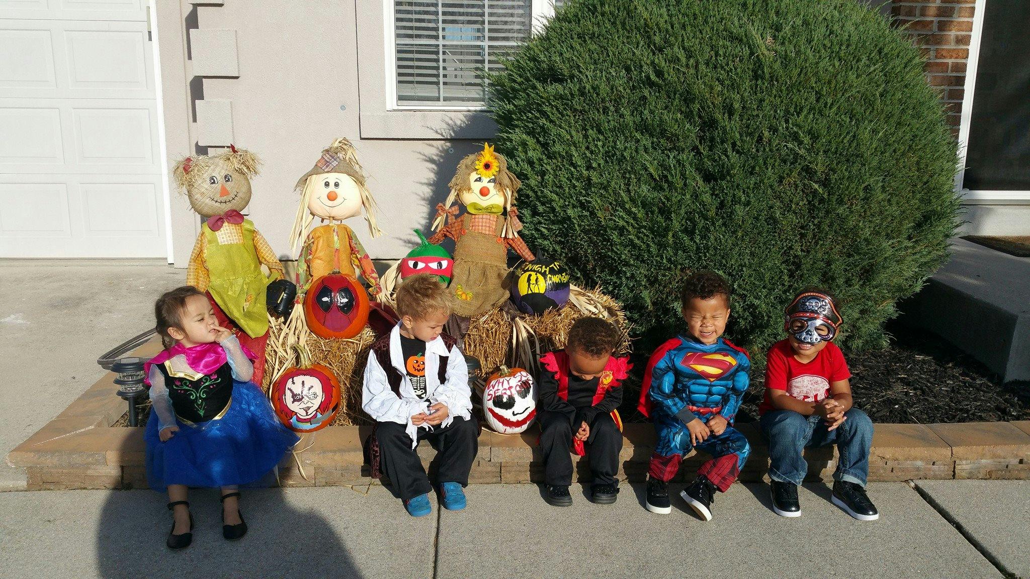 Children in Halloween costumes sitting in front of scarecrows