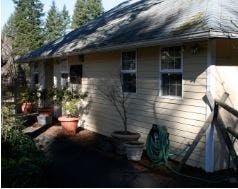 Side of a house with potted plants and a garden hose