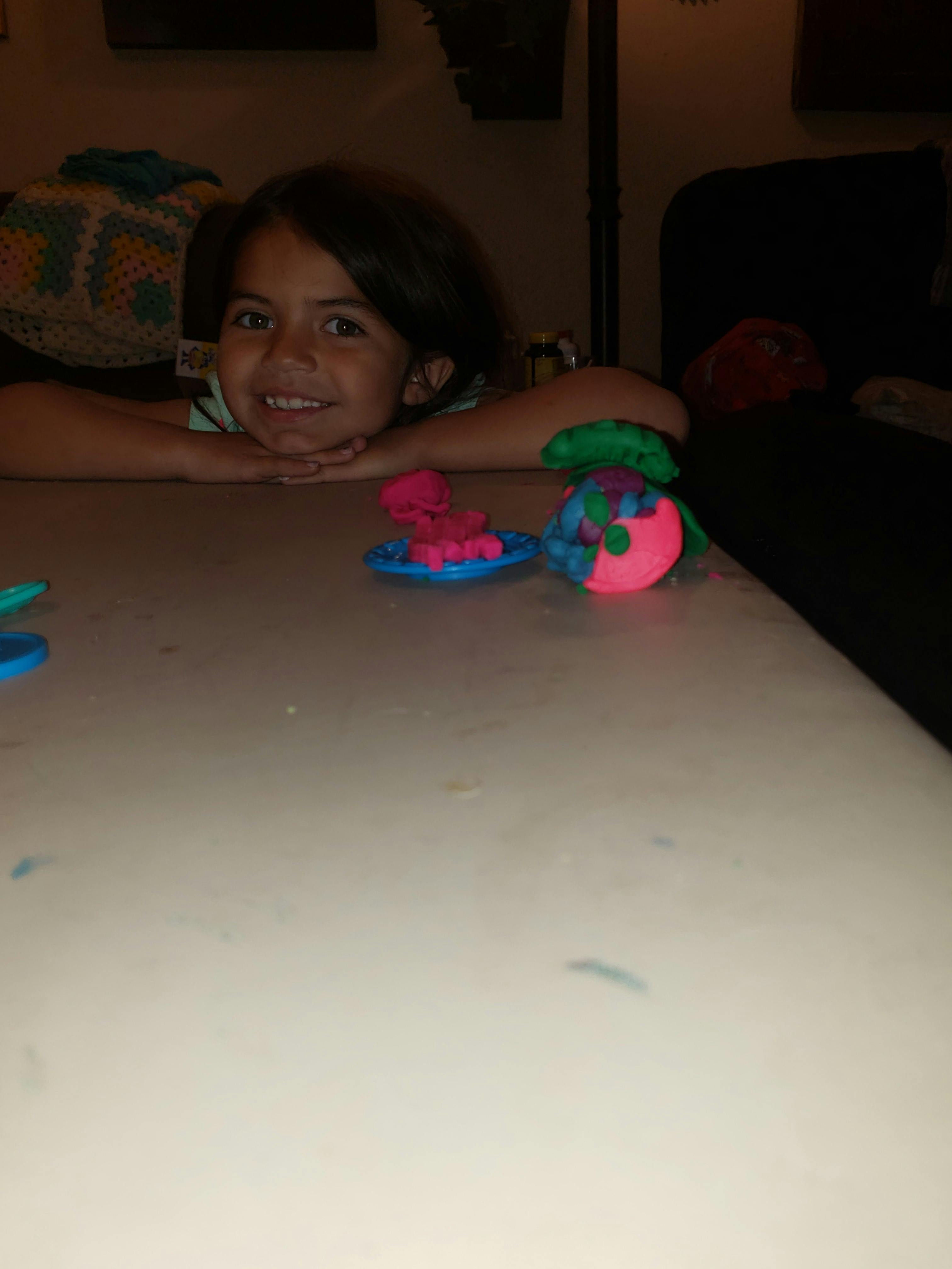 Child resting chin on hands with colorful playdough creations on a table