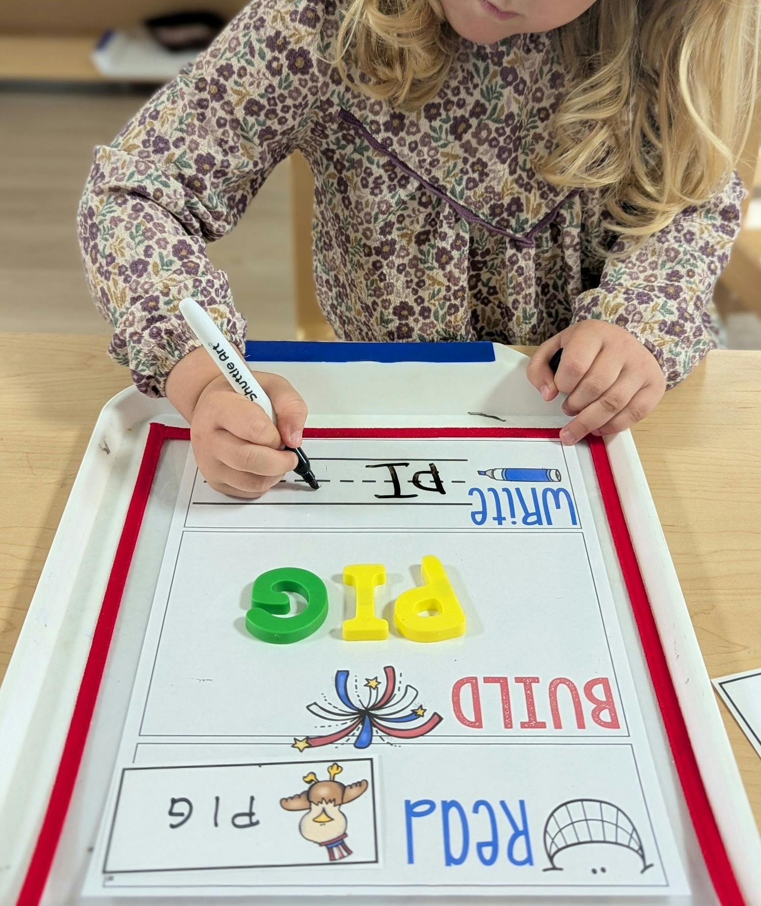 Child writing on a whiteboard with letter tiles