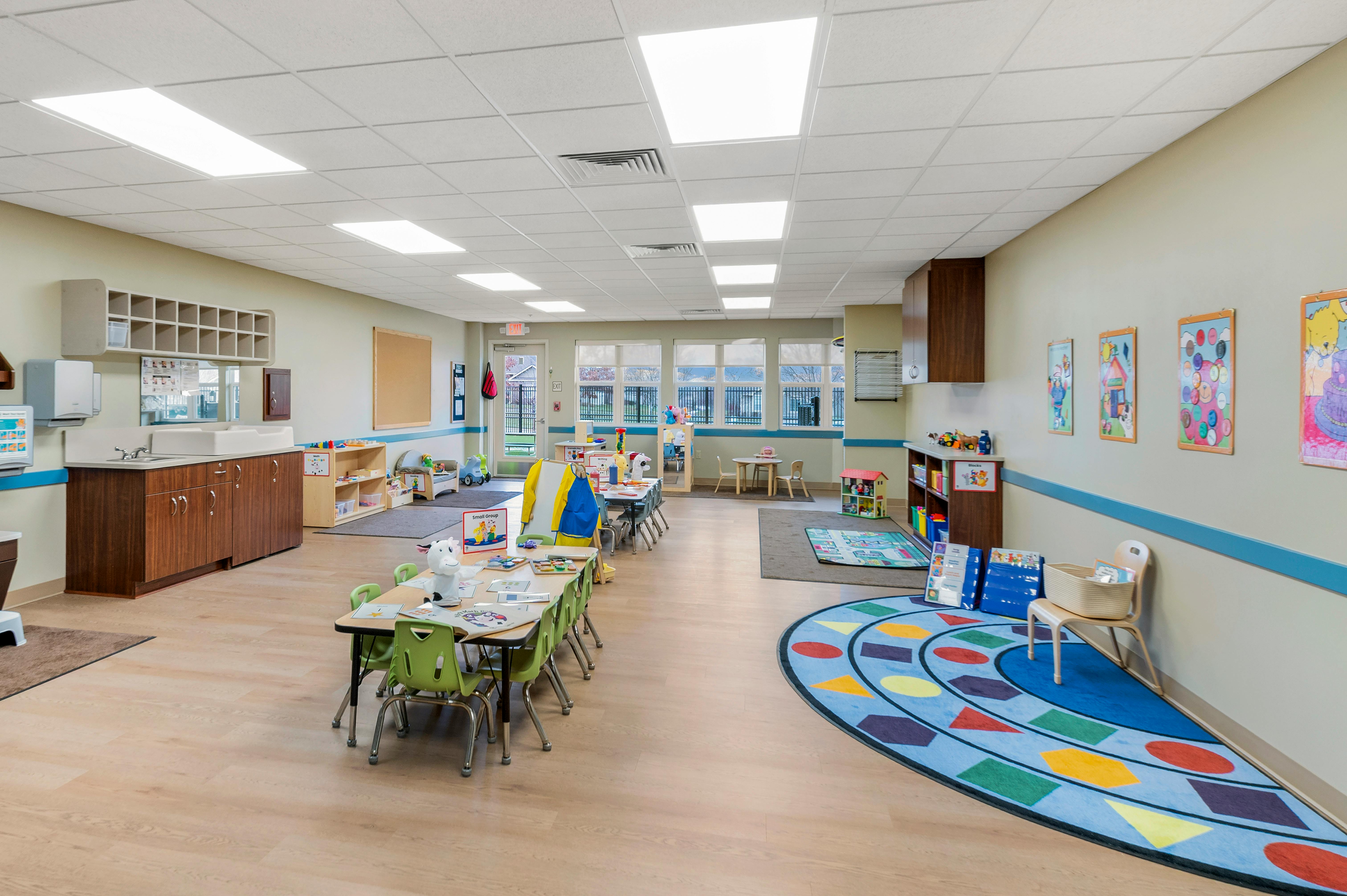 Classroom with small tables and chairs, a changing station, and colorful rugs