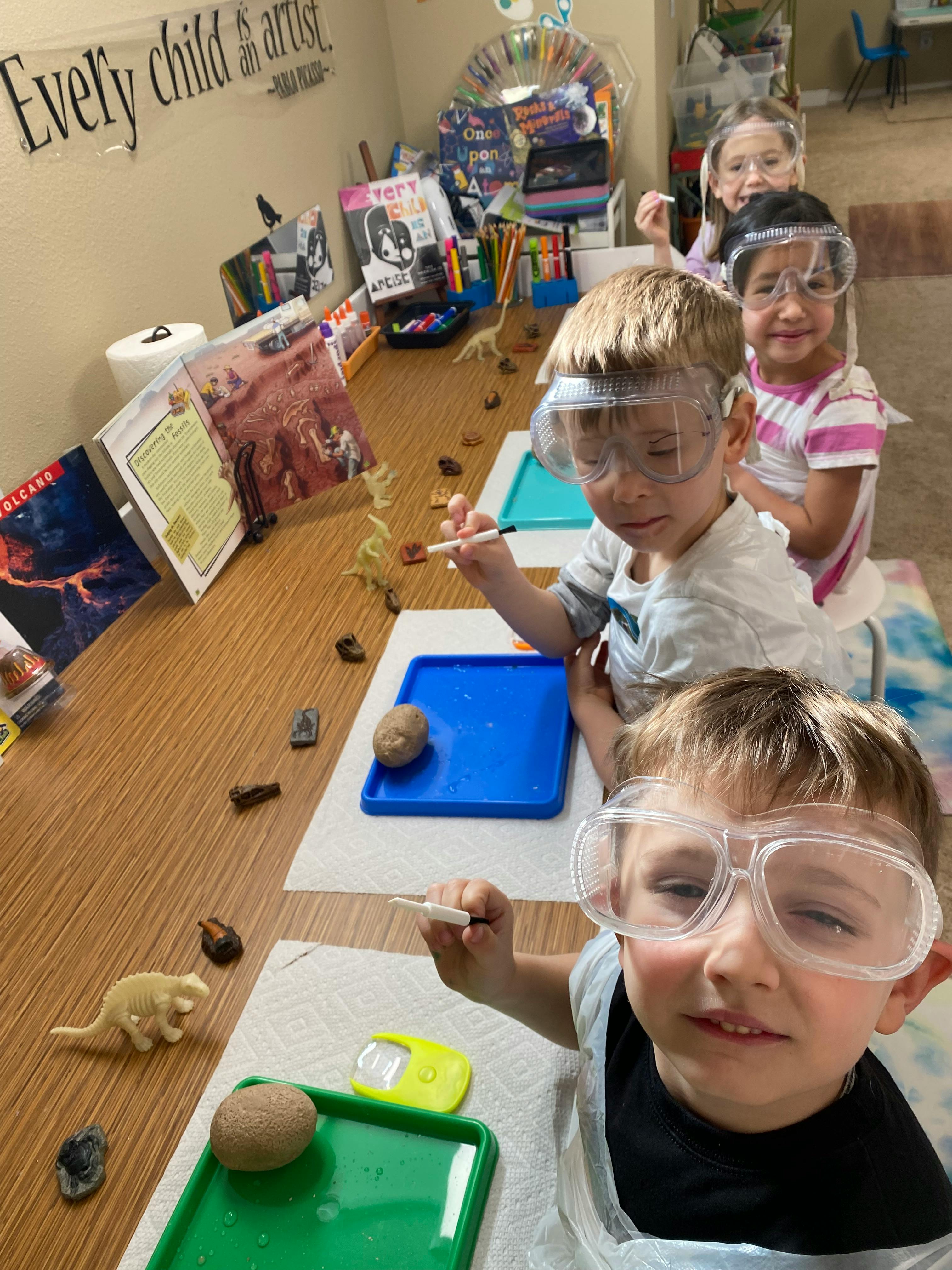 Children wearing safety glasses painting objects at a table