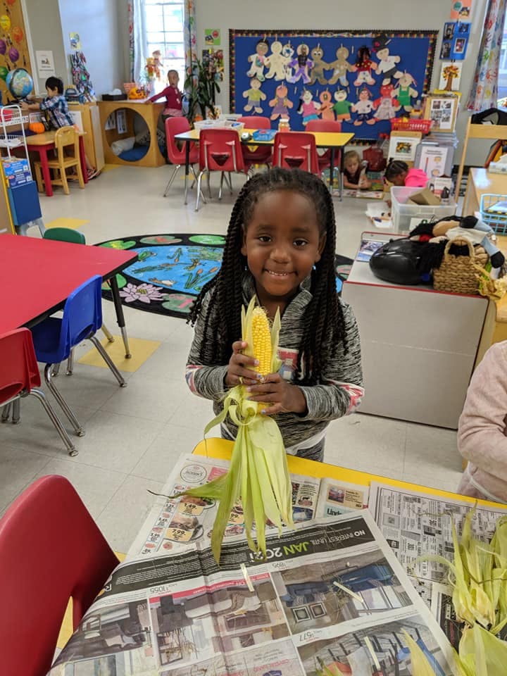 Child holding an ear of corn in a classroom