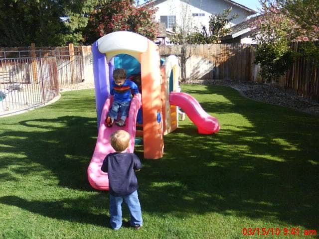 Child on a slide with another child standing nearby