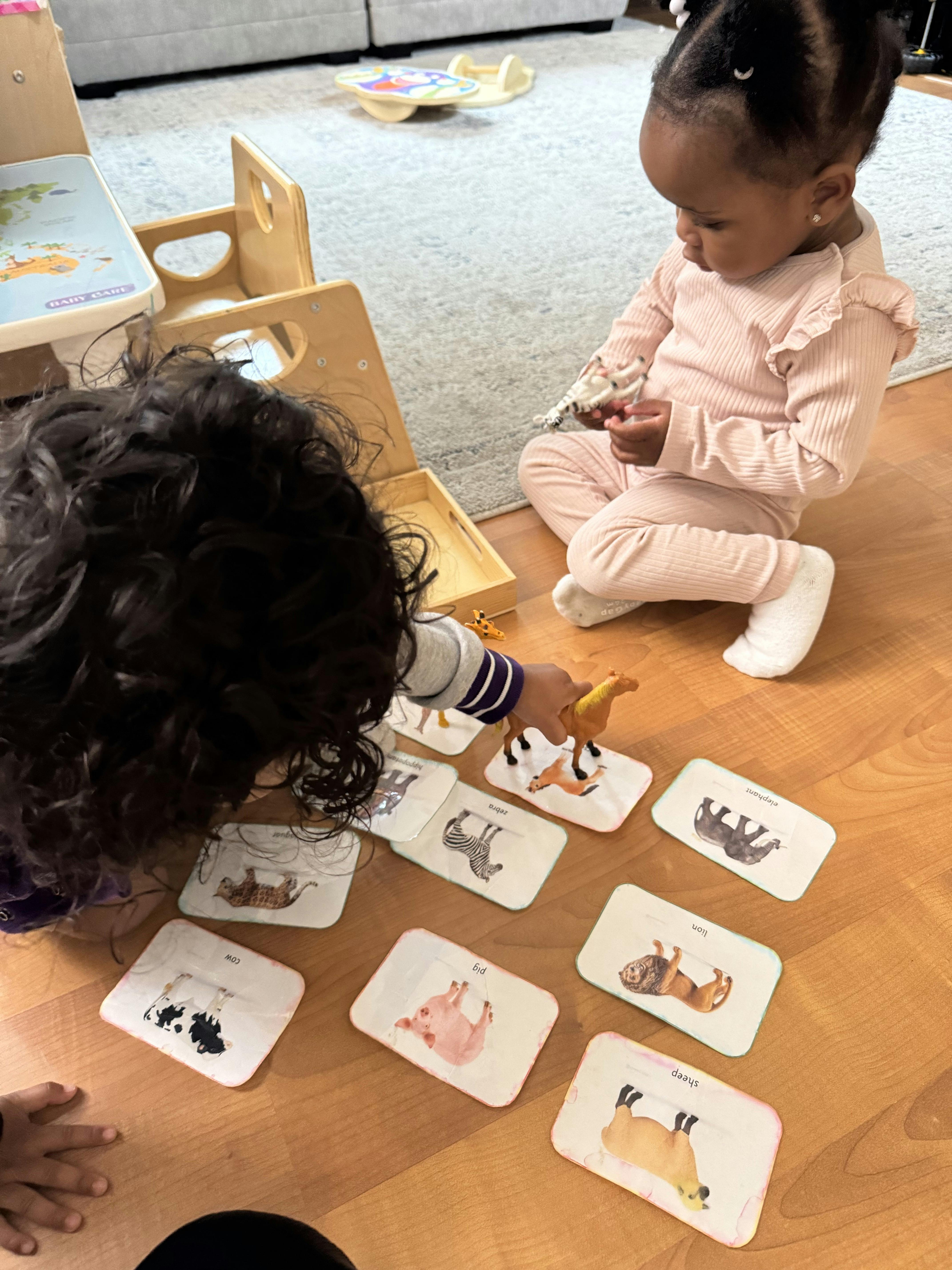Two children playing with animal cards and figurines on a wooden floor