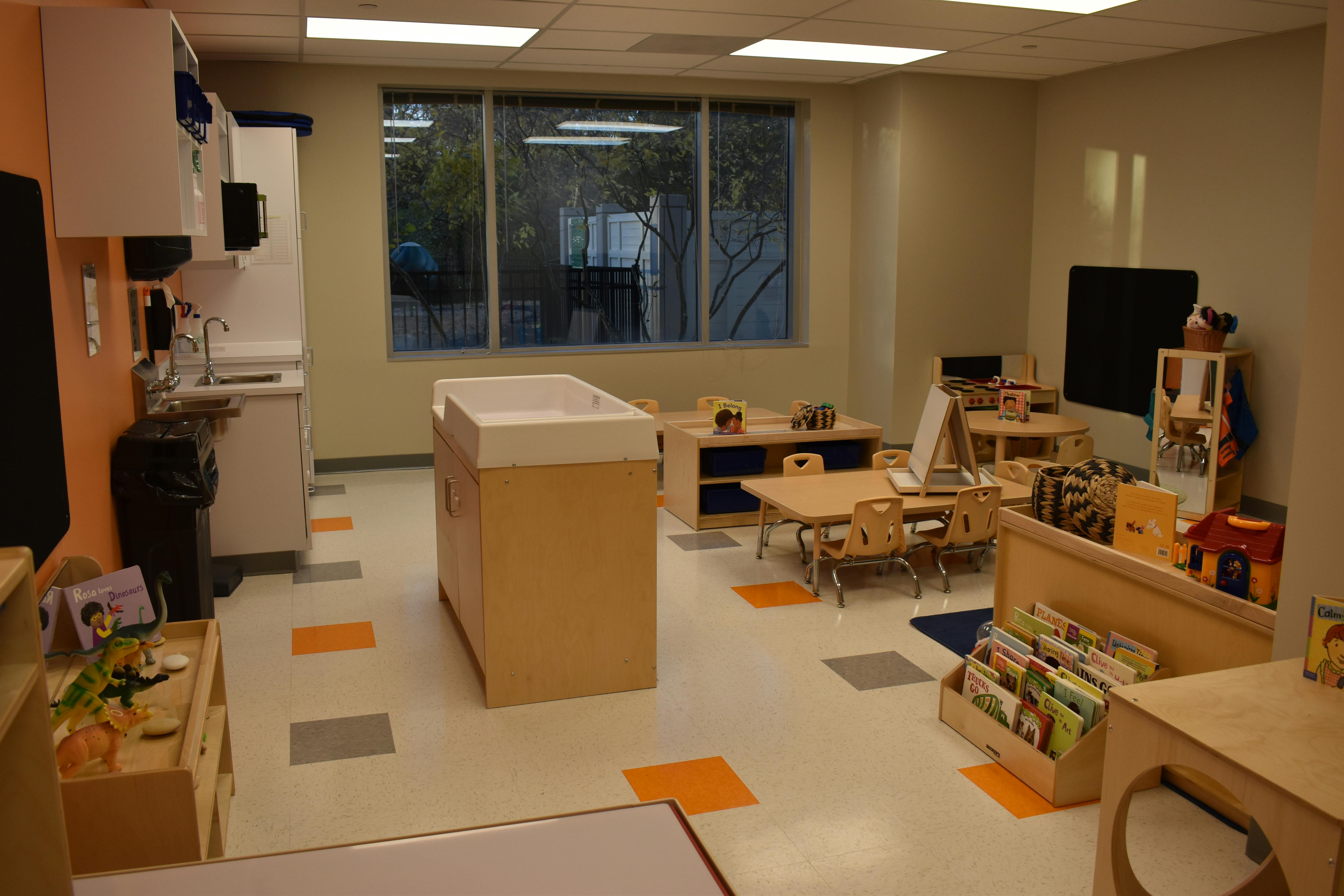 Classroom with small tables and chairs, shelves, and a changing station