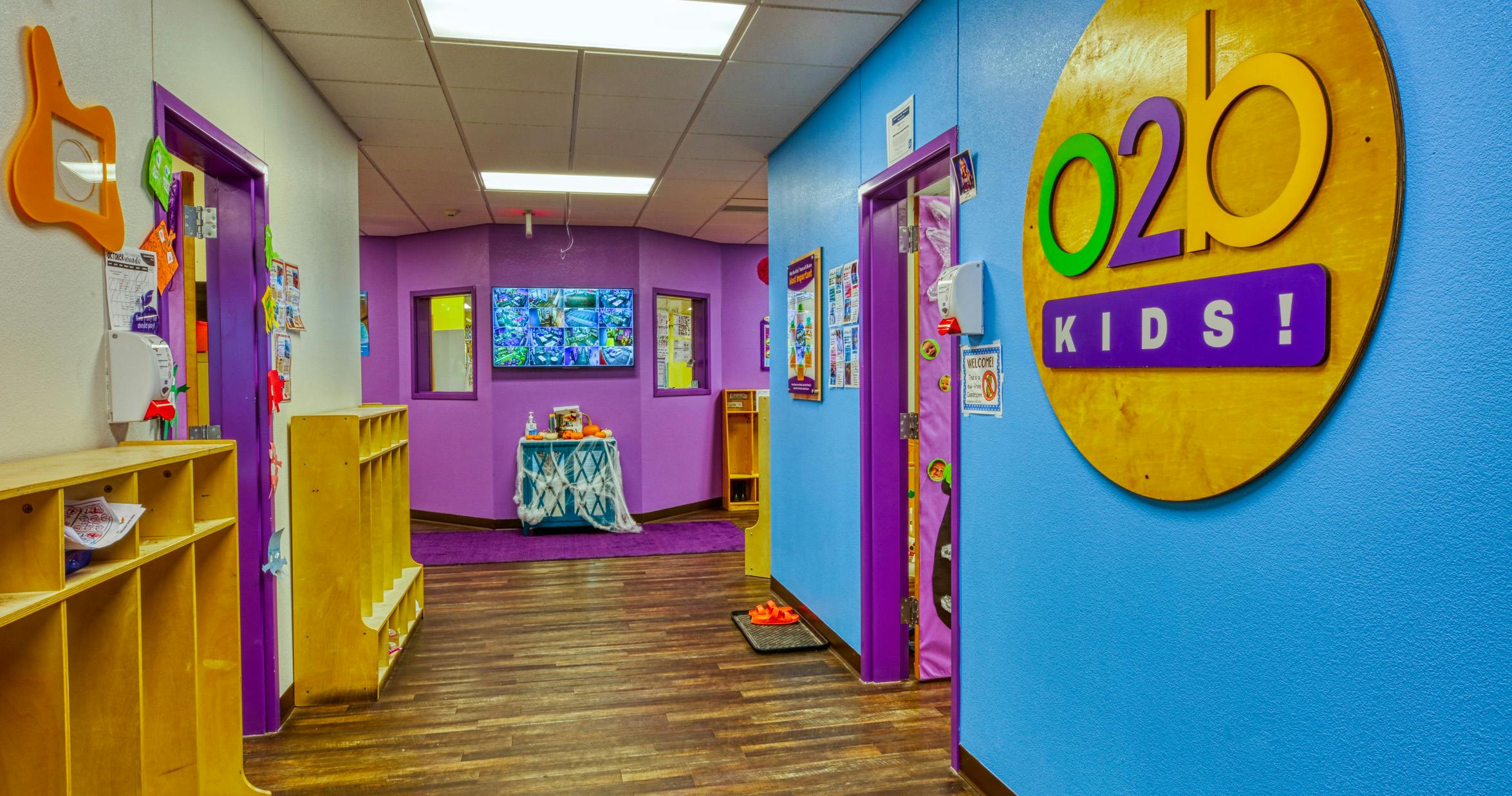 Children's hallway with purple walls, blue wall with "O2B Kids!" sign, and wooden cubbies