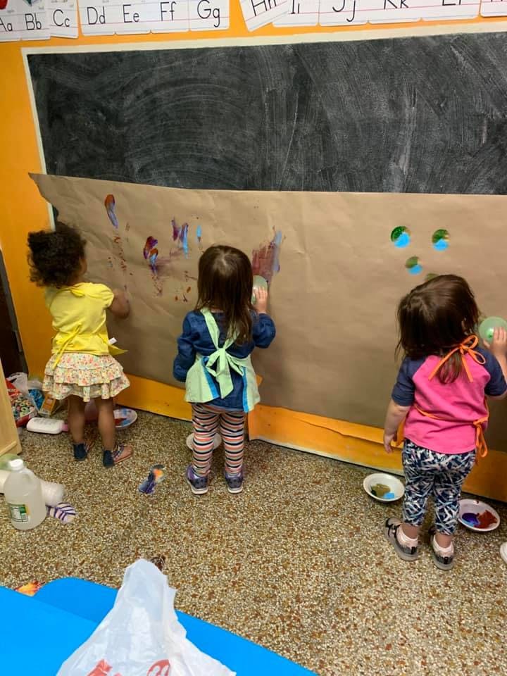 Three children painting on a large sheet of paper in a classroom