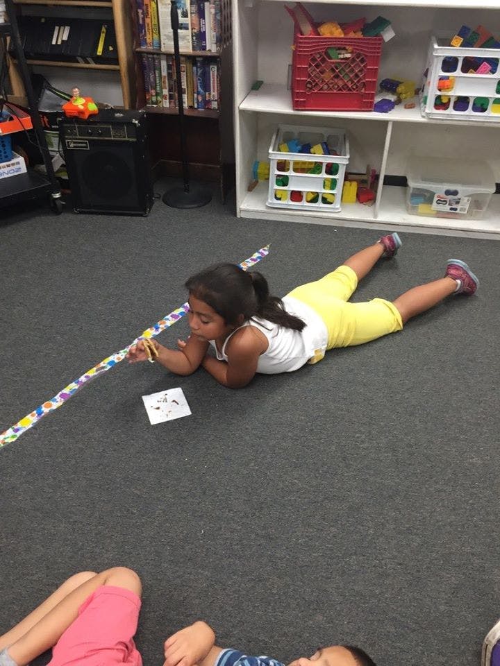 Child lying on floor, looking at a long colorful stick