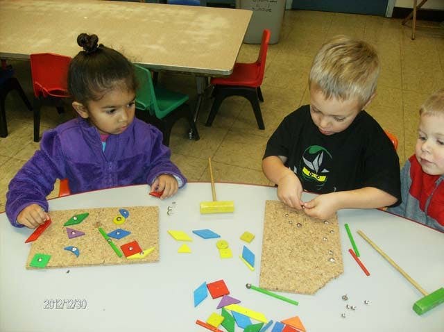 Three children playing with colorful shapes and cork boards at a table