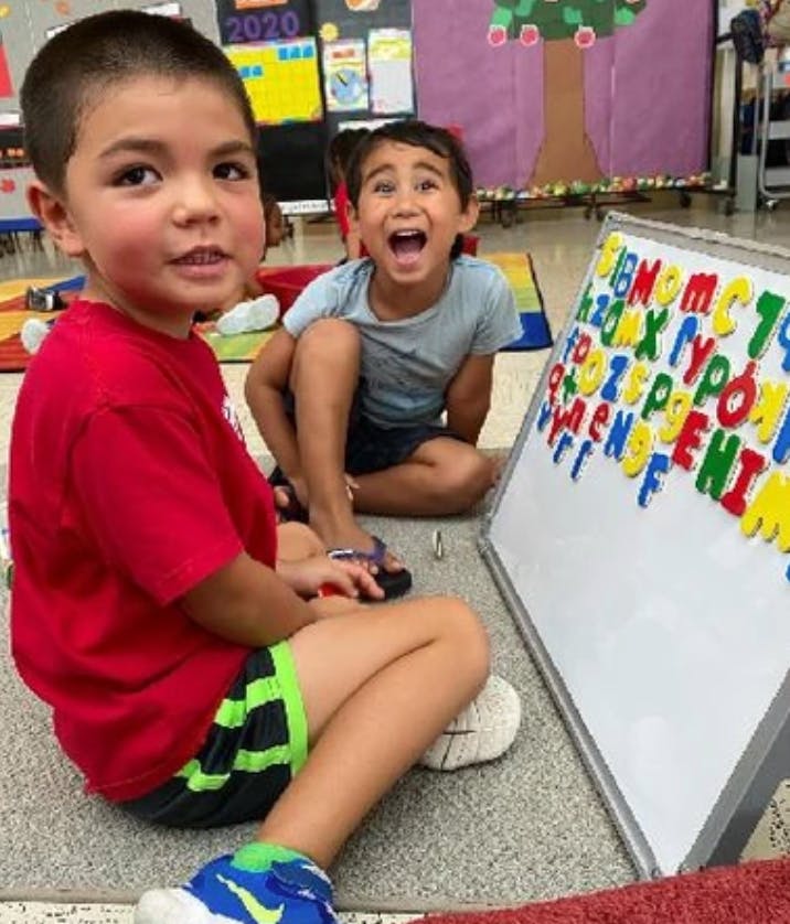 Two children sitting on the floor with a magnetic letter board