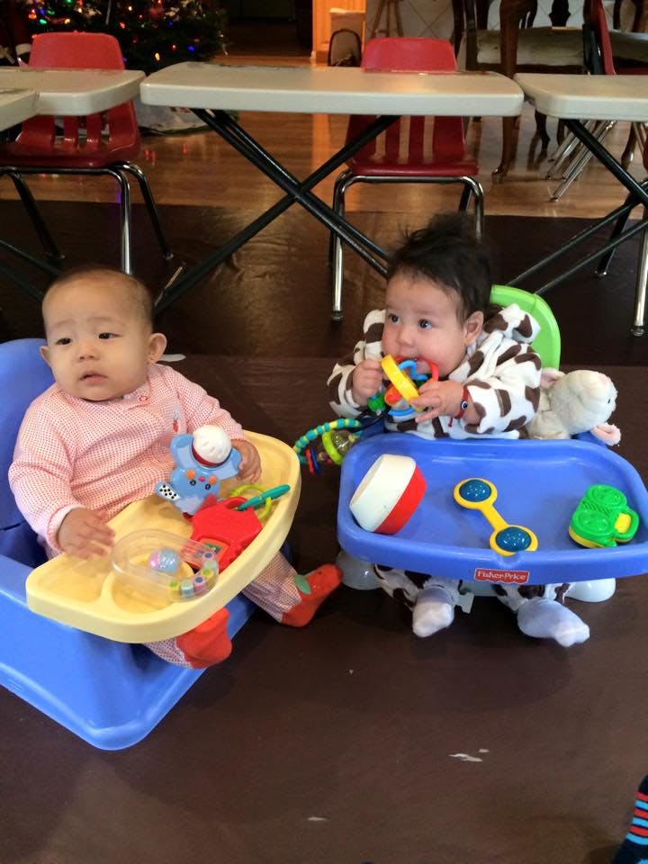 Two babies sitting in high chairs with toys