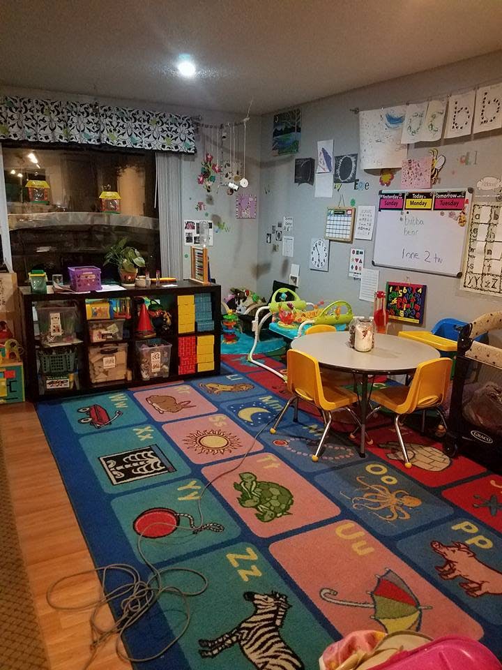 A classroom with a colorful alphabet rug, small table and chairs, and storage shelves