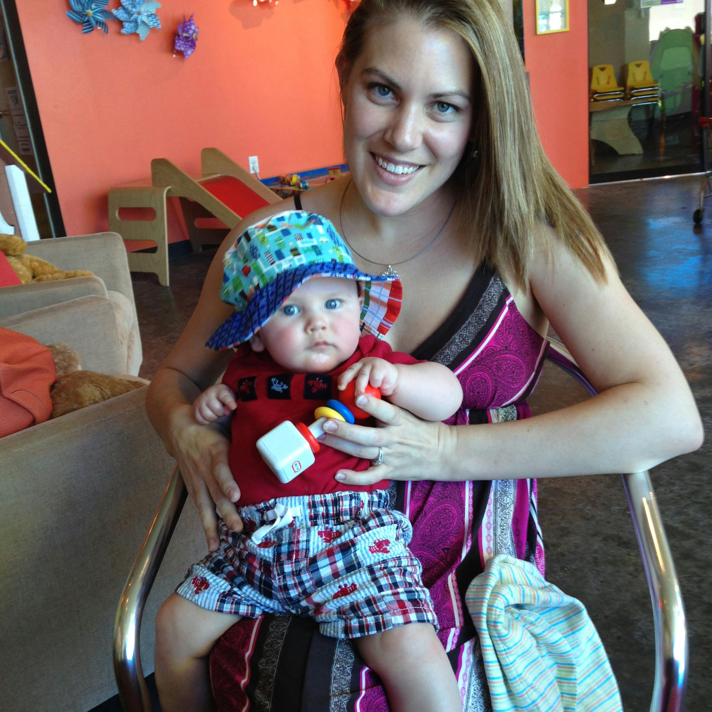 Person holding a child wearing a hat and holding a toy