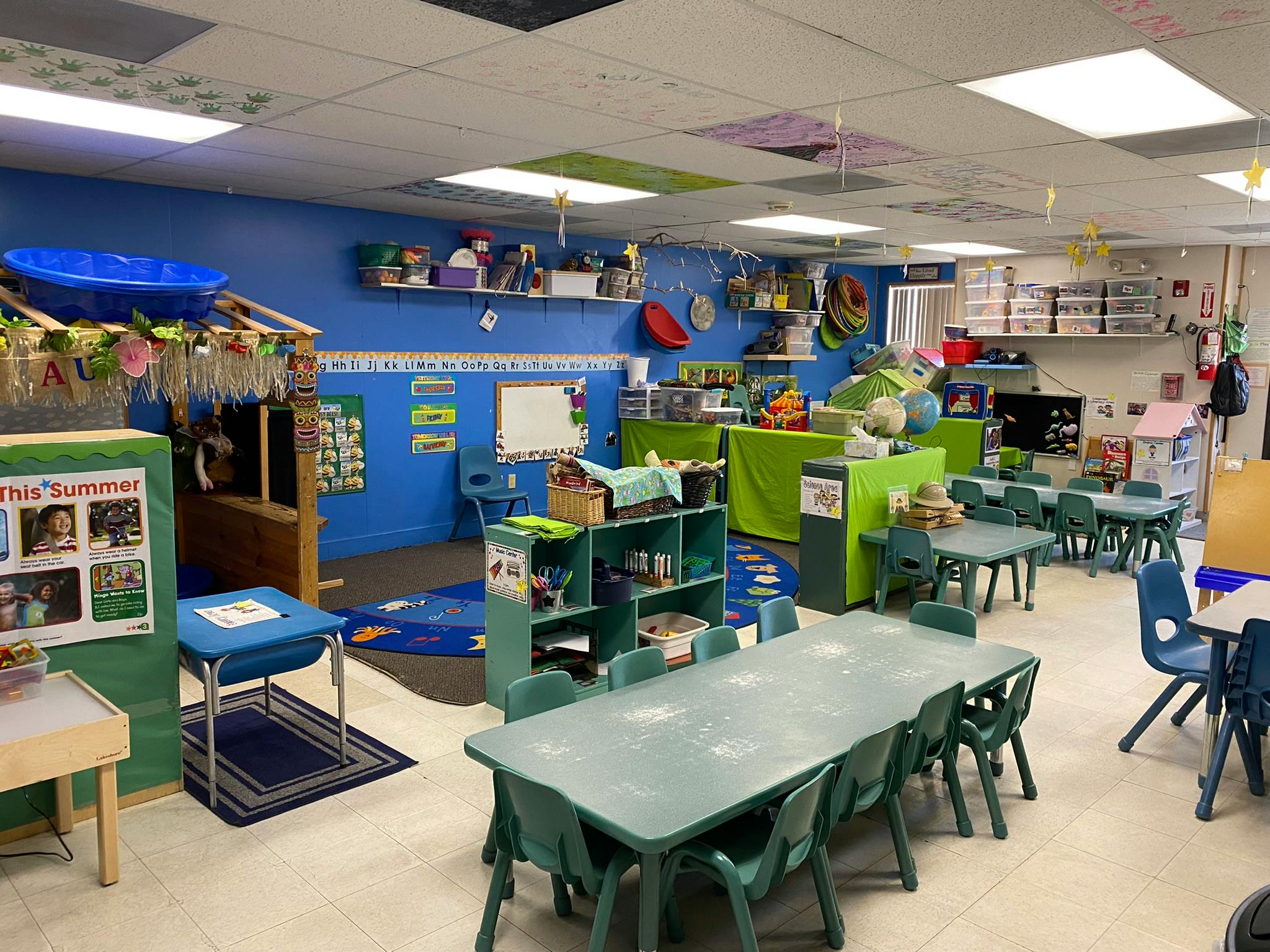Classroom with small tables and chairs, shelves with toys, and posters on blue walls
