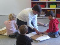 Adult and three children on floor looking at paper