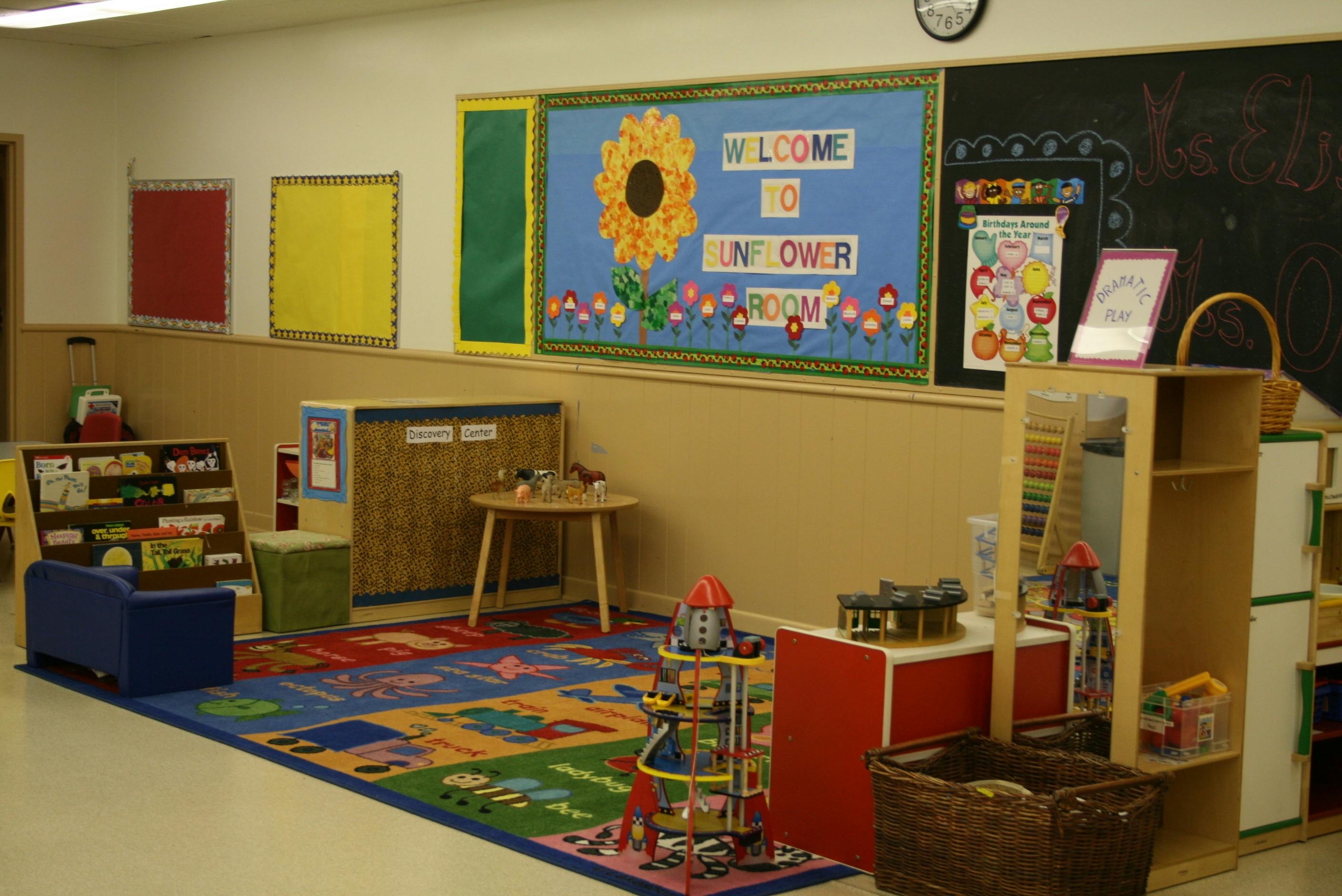 Classroom with a colorful rug, small tables, and a bulletin board with a sunflower