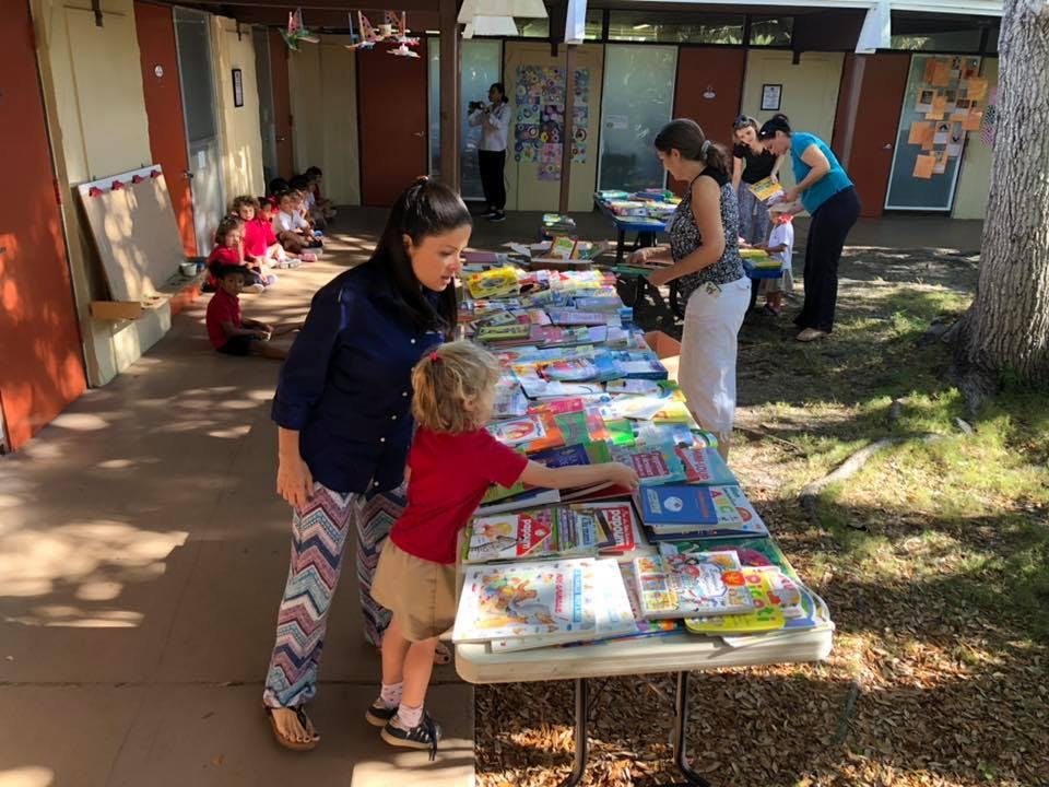 Adult and child looking at books on a table outdoors