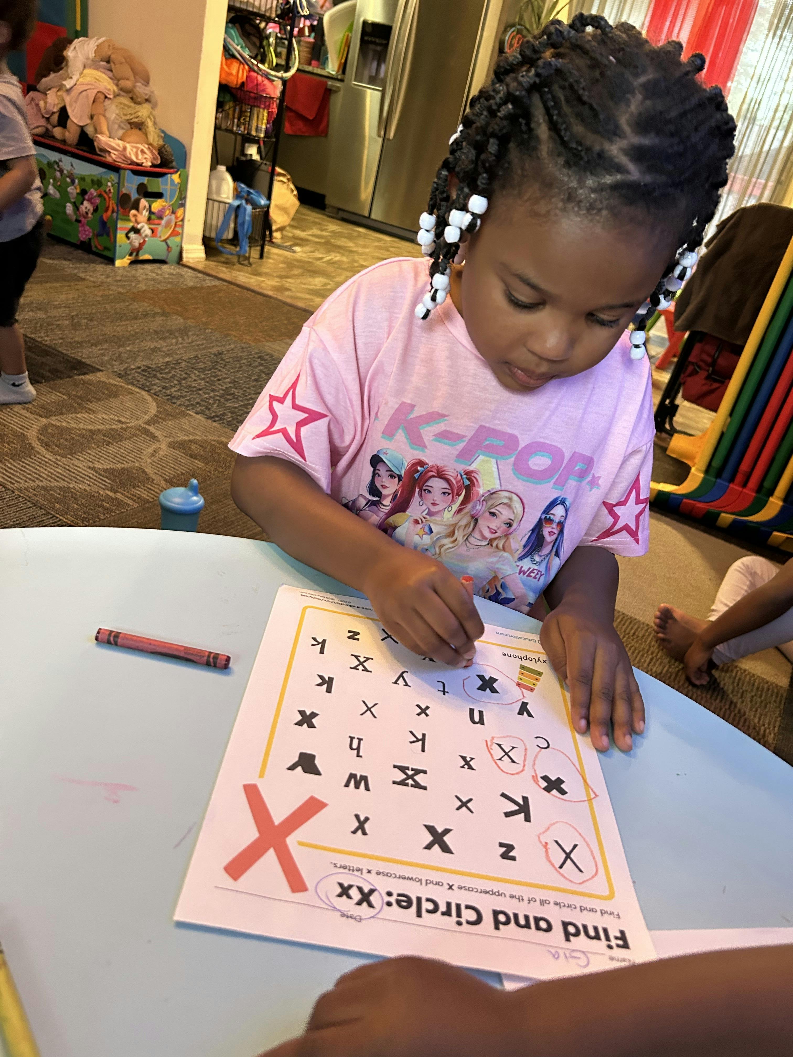 Child circling the letter X on a worksheet at a table
