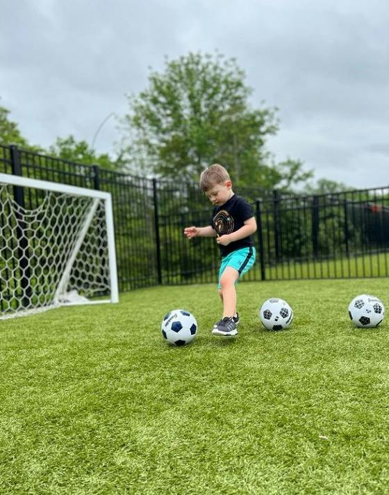 Child on a soccer field with multiple soccer balls and a goal
