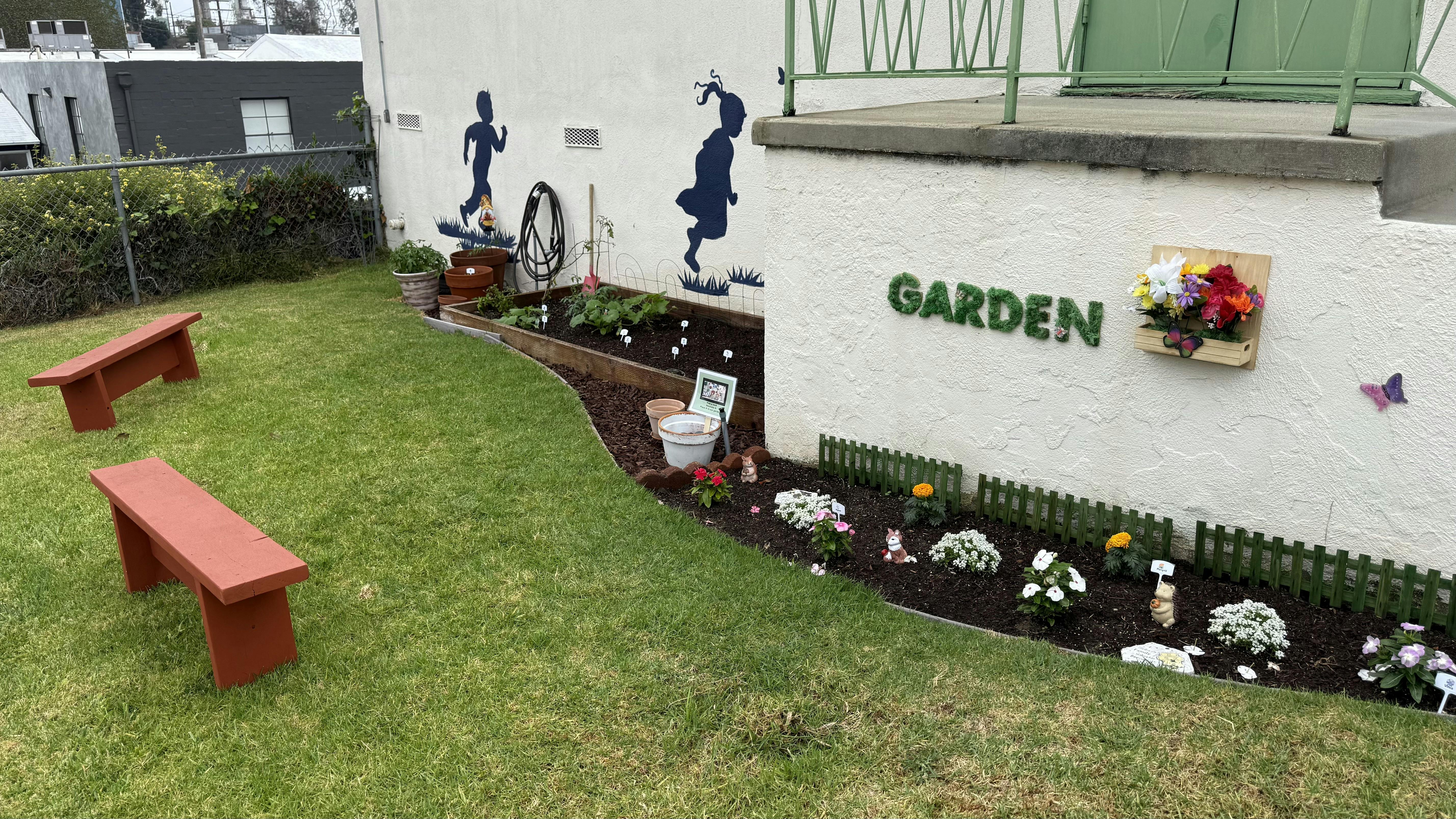Two red benches on grass next to a garden bed with "GARDEN" on a wall